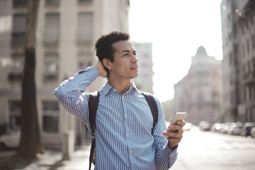 A young male looking confused at his phone in the city.